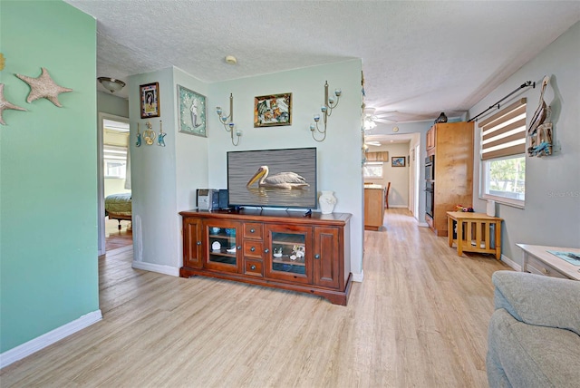 living room with ceiling fan, a textured ceiling, and light hardwood / wood-style flooring