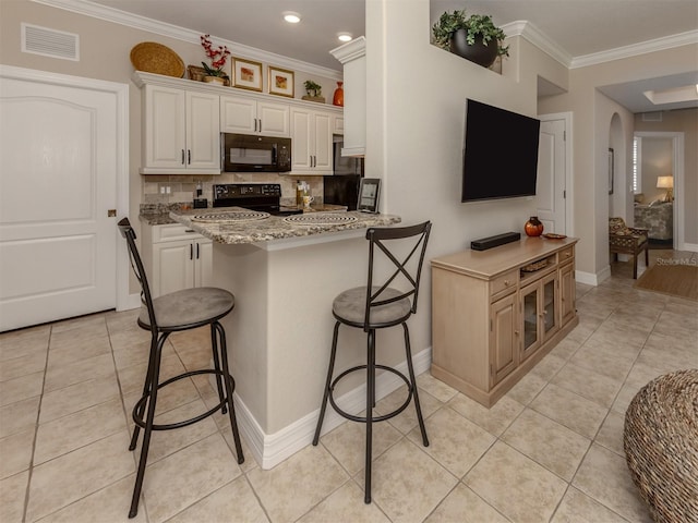 kitchen with white cabinetry, tasteful backsplash, light stone counters, a breakfast bar area, and black appliances