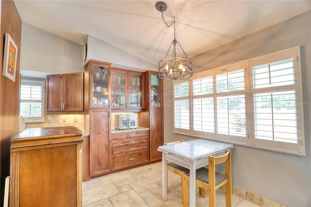 kitchen with a notable chandelier, backsplash, a textured ceiling, vaulted ceiling, and decorative light fixtures