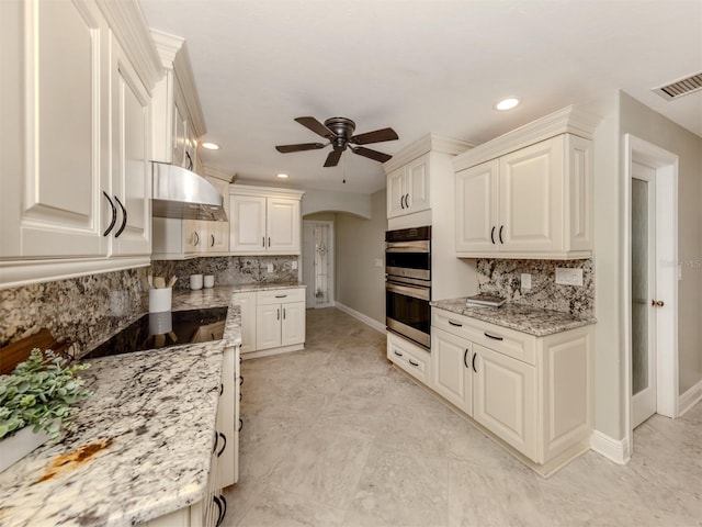 kitchen featuring decorative backsplash, light stone counters, double oven, and ceiling fan