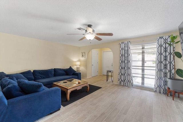 living room featuring ceiling fan, light hardwood / wood-style floors, and a textured ceiling