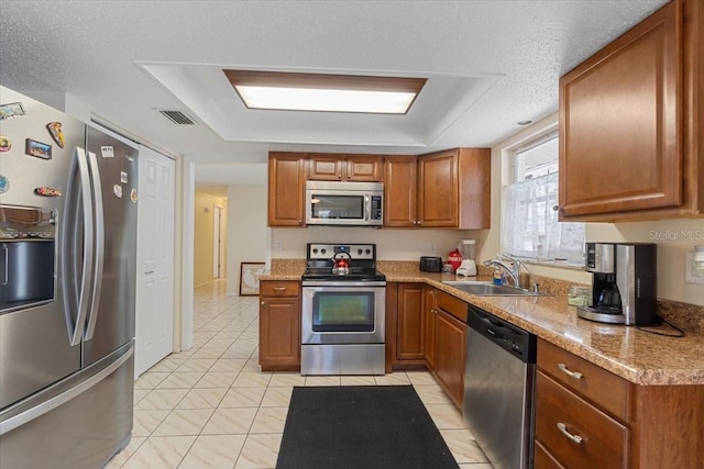 kitchen featuring sink, light stone countertops, a textured ceiling, light tile patterned floors, and stainless steel appliances