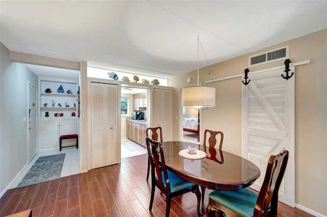 dining room with a barn door, dark hardwood / wood-style flooring, and built in shelves