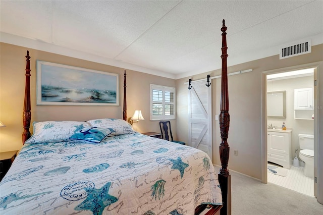 bedroom with light carpet, a barn door, ensuite bathroom, and sink