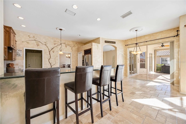 kitchen featuring a kitchen bar, stainless steel fridge with ice dispenser, hanging light fixtures, and ceiling fan