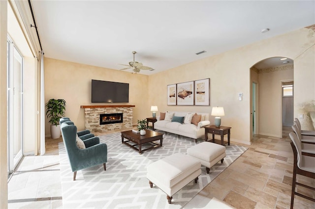 living room with ceiling fan, a healthy amount of sunlight, and a stone fireplace