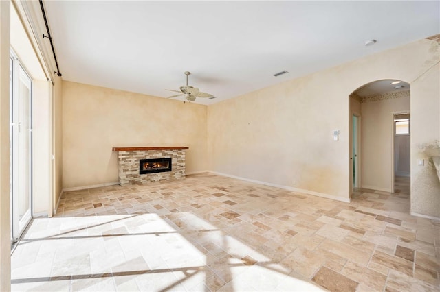 unfurnished living room with a stone fireplace and ceiling fan