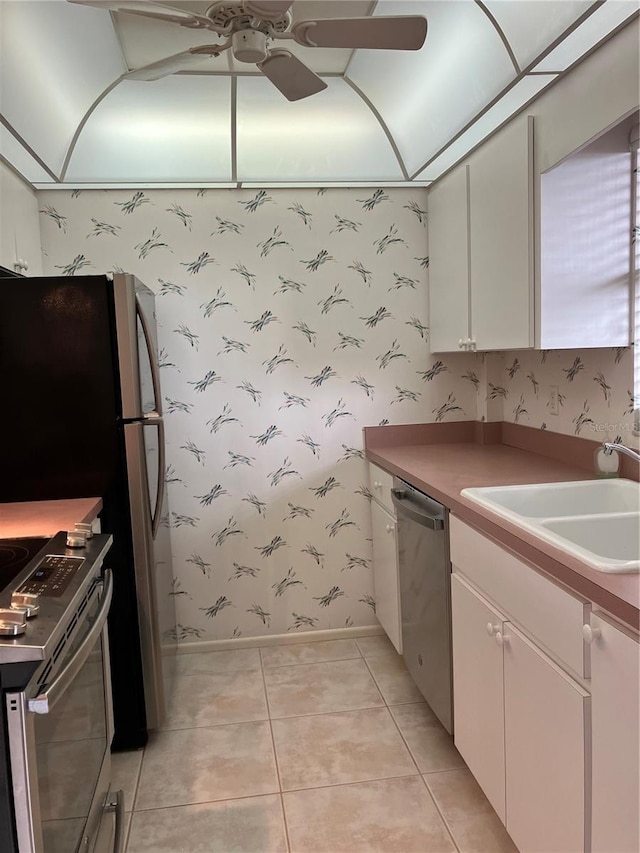 kitchen with sink, light tile patterned floors, appliances with stainless steel finishes, ceiling fan, and white cabinets