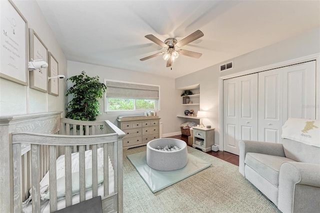 bedroom featuring a closet, wood-type flooring, a nursery area, and ceiling fan