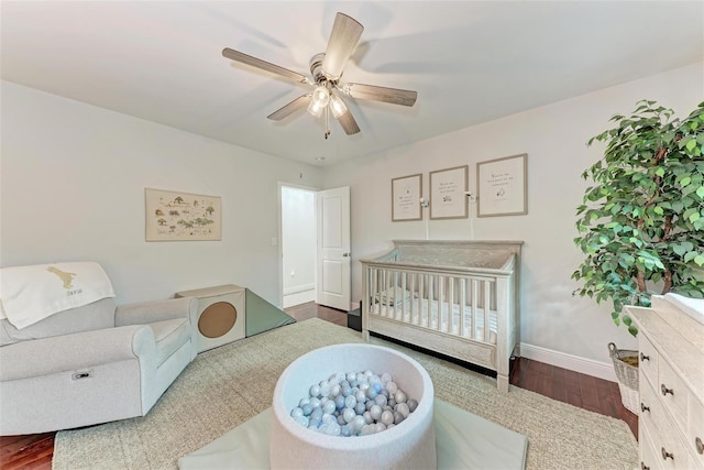 bedroom with dark wood-type flooring, ceiling fan, and a crib