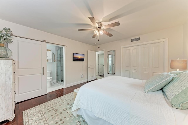 bedroom with a barn door, ceiling fan, ensuite bath, a closet, and dark hardwood / wood-style flooring