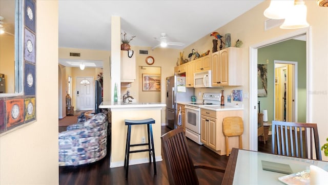 kitchen with ceiling fan, kitchen peninsula, white appliances, a breakfast bar area, and light brown cabinetry