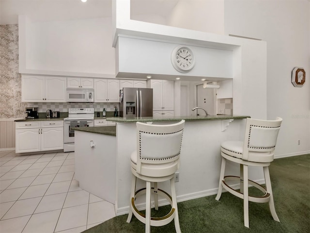 kitchen featuring light tile patterned floors, white appliances, white cabinetry, a kitchen breakfast bar, and kitchen peninsula