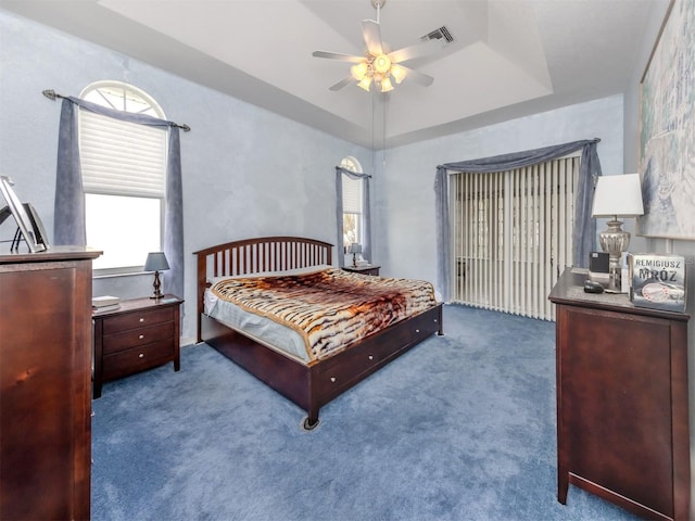 carpeted bedroom with a tray ceiling and ceiling fan