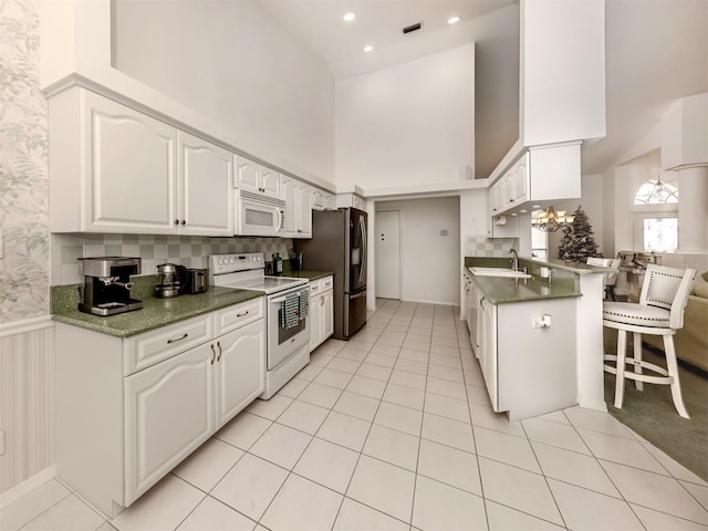 kitchen featuring white cabinetry, white appliances, kitchen peninsula, and a kitchen bar