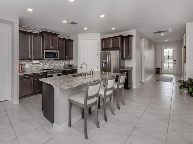 kitchen with light stone counters, stainless steel appliances, an island with sink, a kitchen bar, and sink