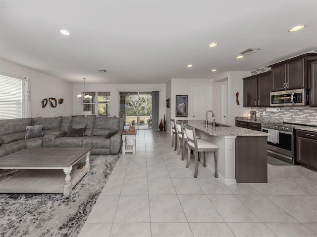 kitchen featuring a kitchen breakfast bar, a center island with sink, an inviting chandelier, appliances with stainless steel finishes, and dark brown cabinets