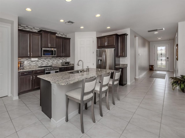 kitchen with a sink, light tile patterned flooring, a breakfast bar area, appliances with stainless steel finishes, and visible vents