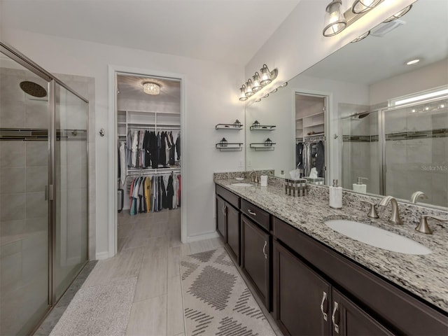full bathroom with a spacious closet, a sink, a shower stall, and double vanity