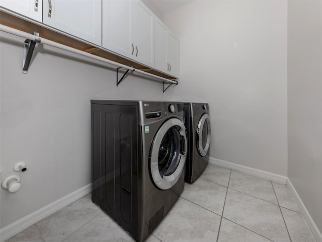 laundry room featuring baseboards, washing machine and clothes dryer, cabinet space, and light tile patterned floors