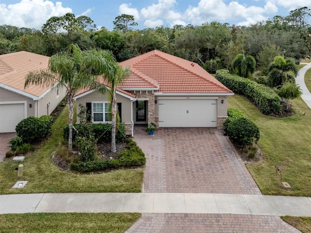 mediterranean / spanish-style house featuring decorative driveway, a tiled roof, an attached garage, a front yard, and stucco siding