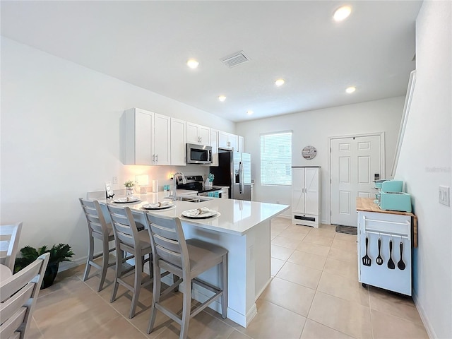 kitchen with a breakfast bar area, light tile patterned floors, white cabinetry, kitchen peninsula, and stainless steel appliances