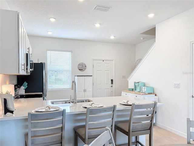 kitchen with kitchen peninsula, refrigerator, sink, white cabinets, and a breakfast bar area