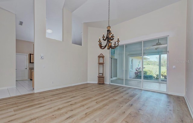 empty room with a notable chandelier, a towering ceiling, and light wood-type flooring