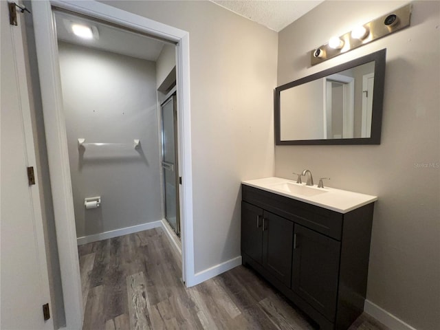 full bathroom with wood finished floors, a shower stall, baseboards, and vanity