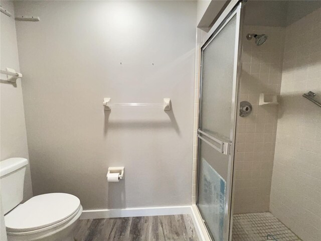 bathroom featuring baseboards, a shower stall, toilet, and wood finished floors