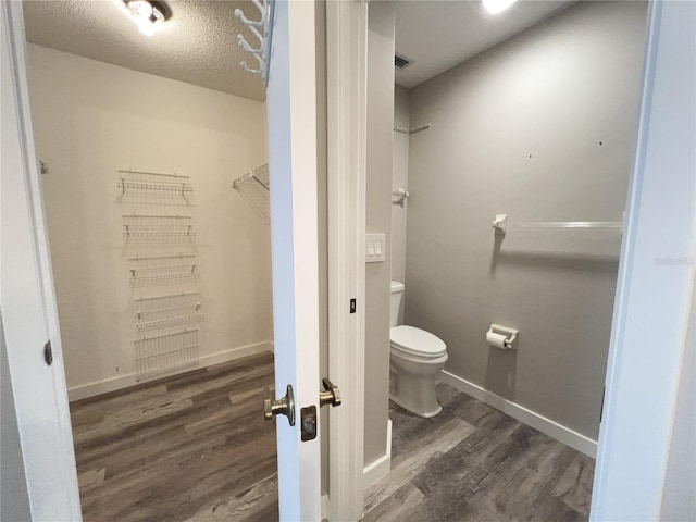 bathroom with visible vents, toilet, a textured ceiling, wood finished floors, and baseboards