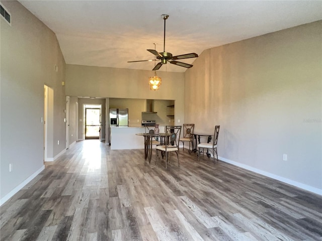 dining space with high vaulted ceiling, a ceiling fan, baseboards, and wood finished floors