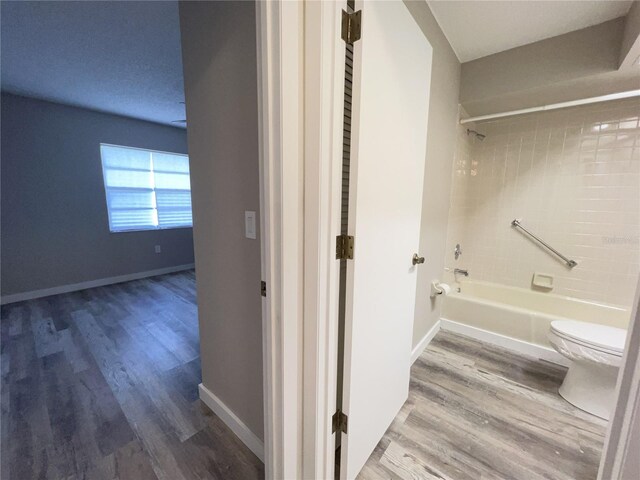 bathroom featuring washtub / shower combination, wood finished floors, toilet, and baseboards