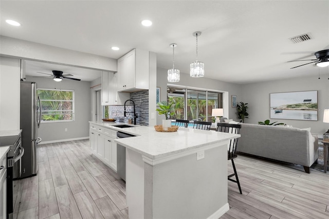 kitchen with a breakfast bar, stainless steel appliances, sink, white cabinets, and hanging light fixtures