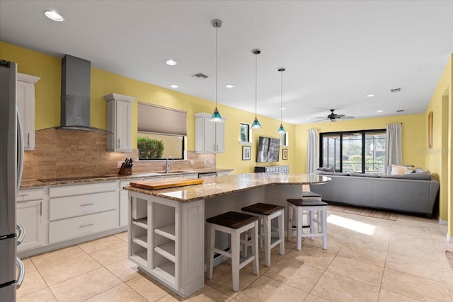 kitchen featuring white cabinetry, wall chimney exhaust hood, light stone countertops, and a kitchen island