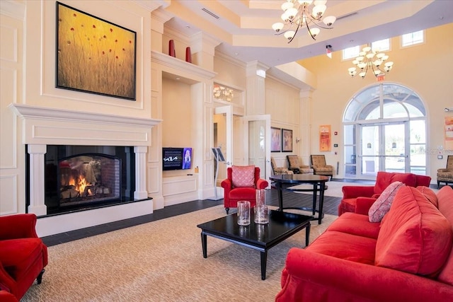 living room featuring a raised ceiling, crown molding, a high ceiling, and a notable chandelier