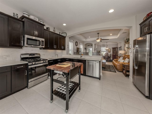 kitchen with light tile patterned floors, kitchen peninsula, appliances with stainless steel finishes, a raised ceiling, and dark brown cabinetry