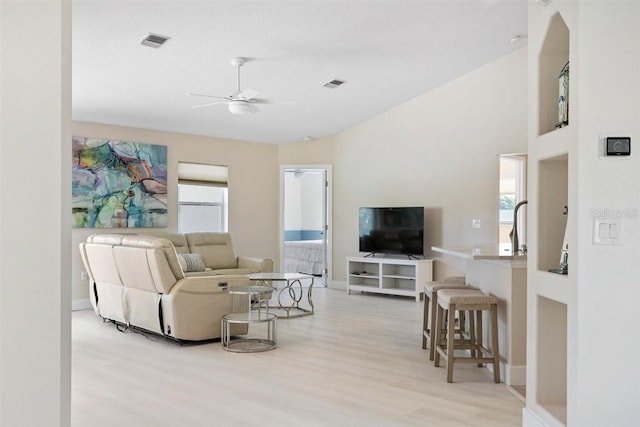 living room with a textured ceiling, light hardwood / wood-style floors, ceiling fan, and lofted ceiling