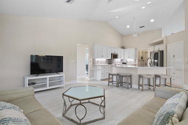 living room featuring ceiling fan, light hardwood / wood-style flooring, high vaulted ceiling, and sink