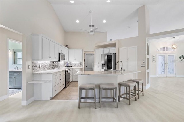 kitchen with white cabinetry, stainless steel appliances, high vaulted ceiling, and an island with sink