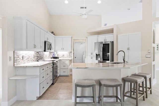 kitchen with appliances with stainless steel finishes, sink, light tile patterned floors, white cabinets, and a high ceiling