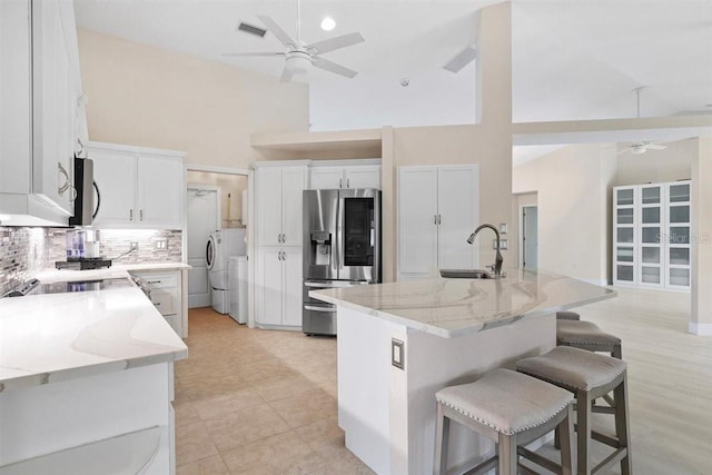 kitchen featuring a kitchen island with sink, white cabinets, stainless steel refrigerator with ice dispenser, and high vaulted ceiling