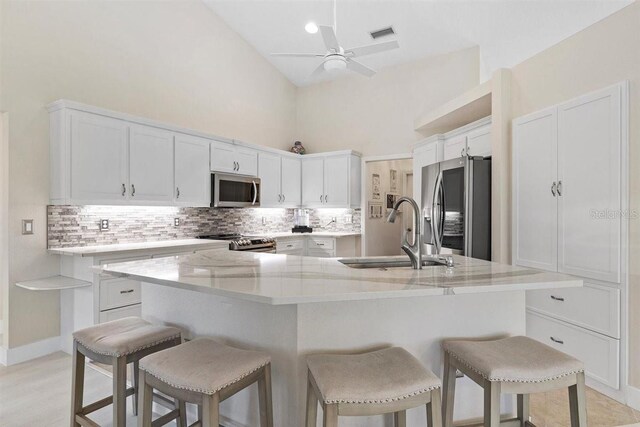 kitchen with stainless steel appliances, a kitchen island with sink, sink, high vaulted ceiling, and white cabinets