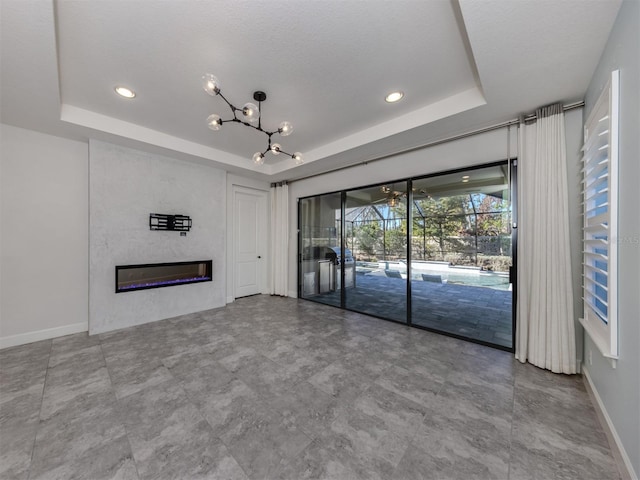 unfurnished living room with baseboards, a chandelier, a tray ceiling, recessed lighting, and a glass covered fireplace