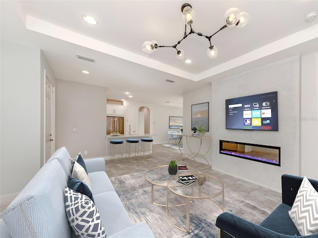 living room featuring visible vents, a tray ceiling, recessed lighting, arched walkways, and a glass covered fireplace