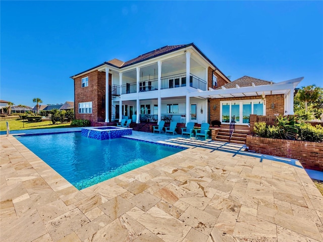 rear view of property featuring a swimming pool with hot tub, a balcony, and a patio