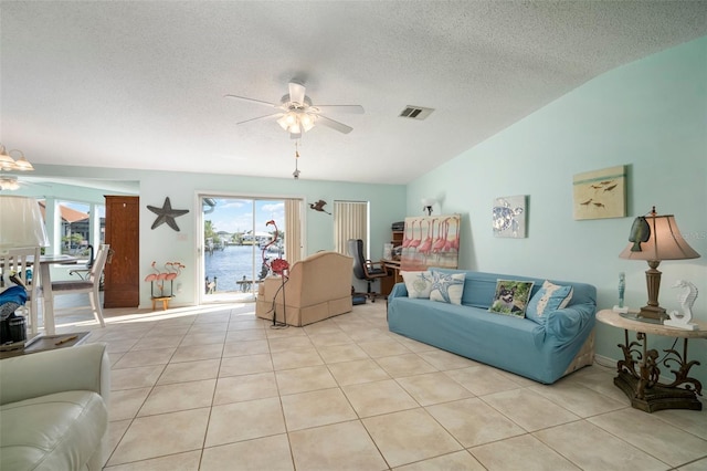 tiled living room with vaulted ceiling, ceiling fan, a water view, and a textured ceiling