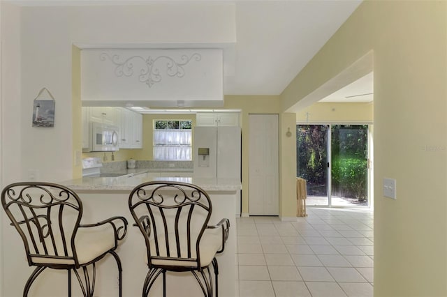 kitchen with white cabinets, light stone counters, white appliances, and kitchen peninsula