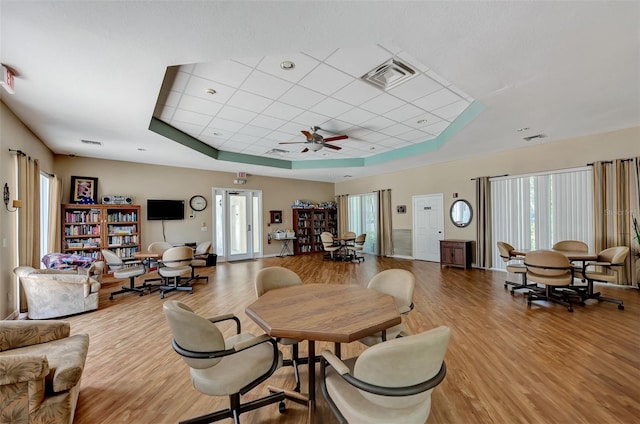 dining space featuring ceiling fan, a drop ceiling, light hardwood / wood-style flooring, and a tray ceiling