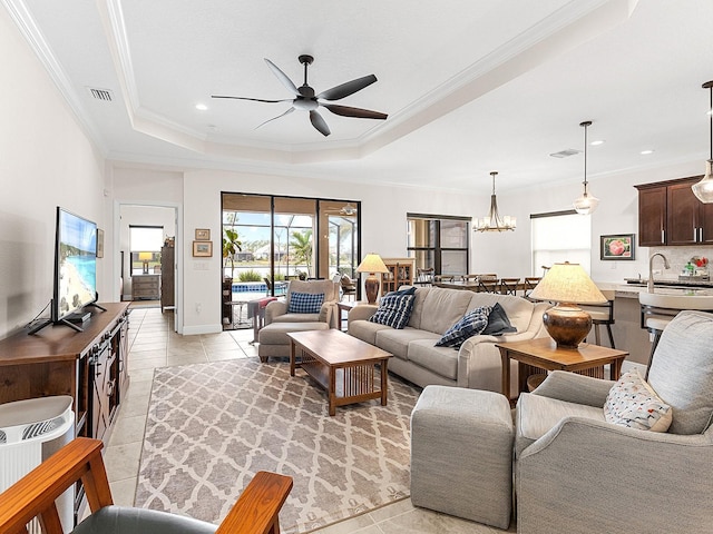 tiled living room with a tray ceiling, crown molding, sink, and ceiling fan with notable chandelier